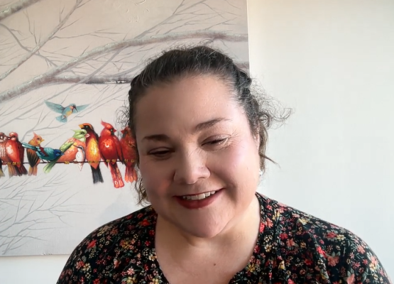 Woman with dark hair smiles on zoom screen with picture or birds behind