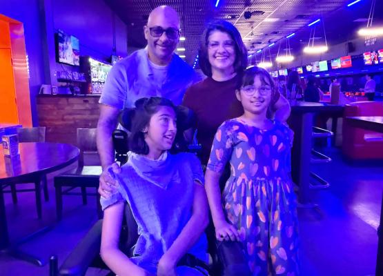 Girl in wheelchair with another girl beside her and man and woman behind in bowling alley