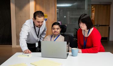 Three people having a meeting, facing a laptop computer