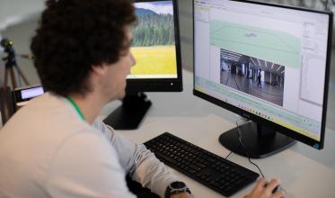 Person looking at a computer which is displaying a video of a person walking while motion capture cameras are tracking their movement.