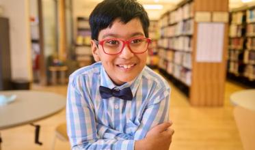 A child wearing glasses crossing the arms with a library background
