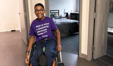 A teenager on wheelchair wearing a happy face in front of a room