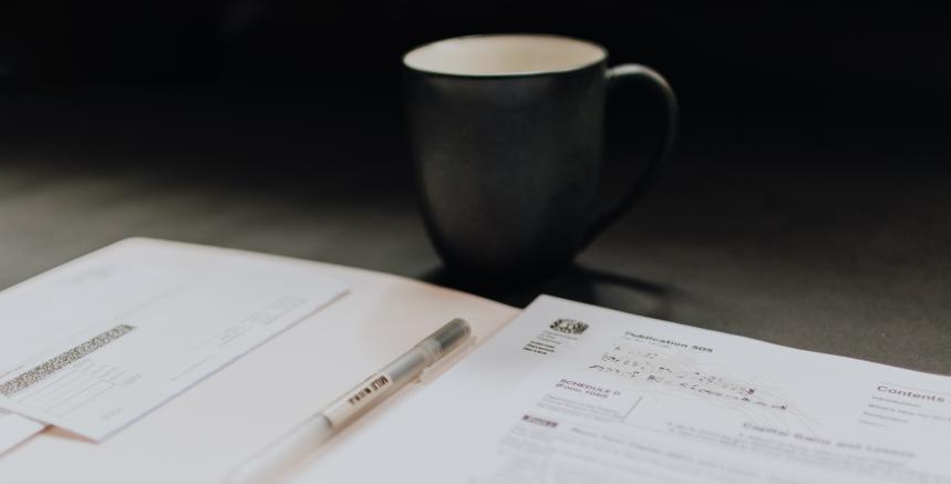 An application form and pen with a mug of tea or coffee in the background