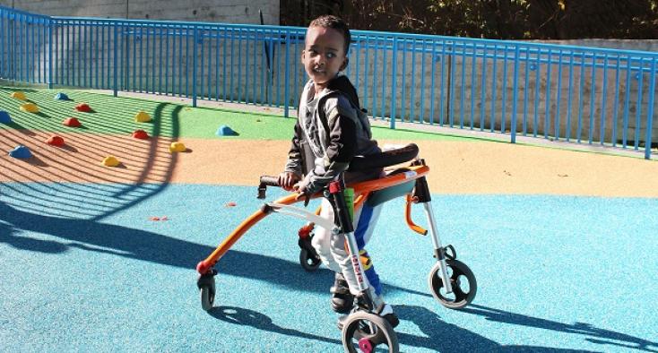 child smiling using a walker in the playground