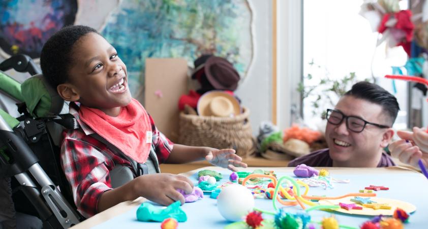 A little boy in a wheel chair playing with arts and crafts at a table