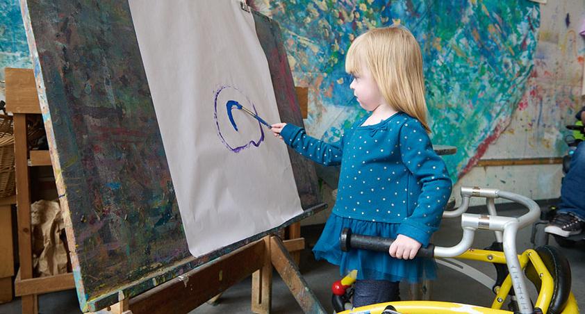 A child holding a wheelchair with one hand, and painting on the other hand