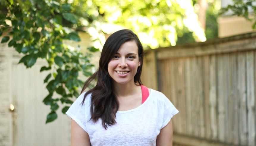 A woman with brown hair wearing a white t-shirt with a pink tank top strap on the right shoulder