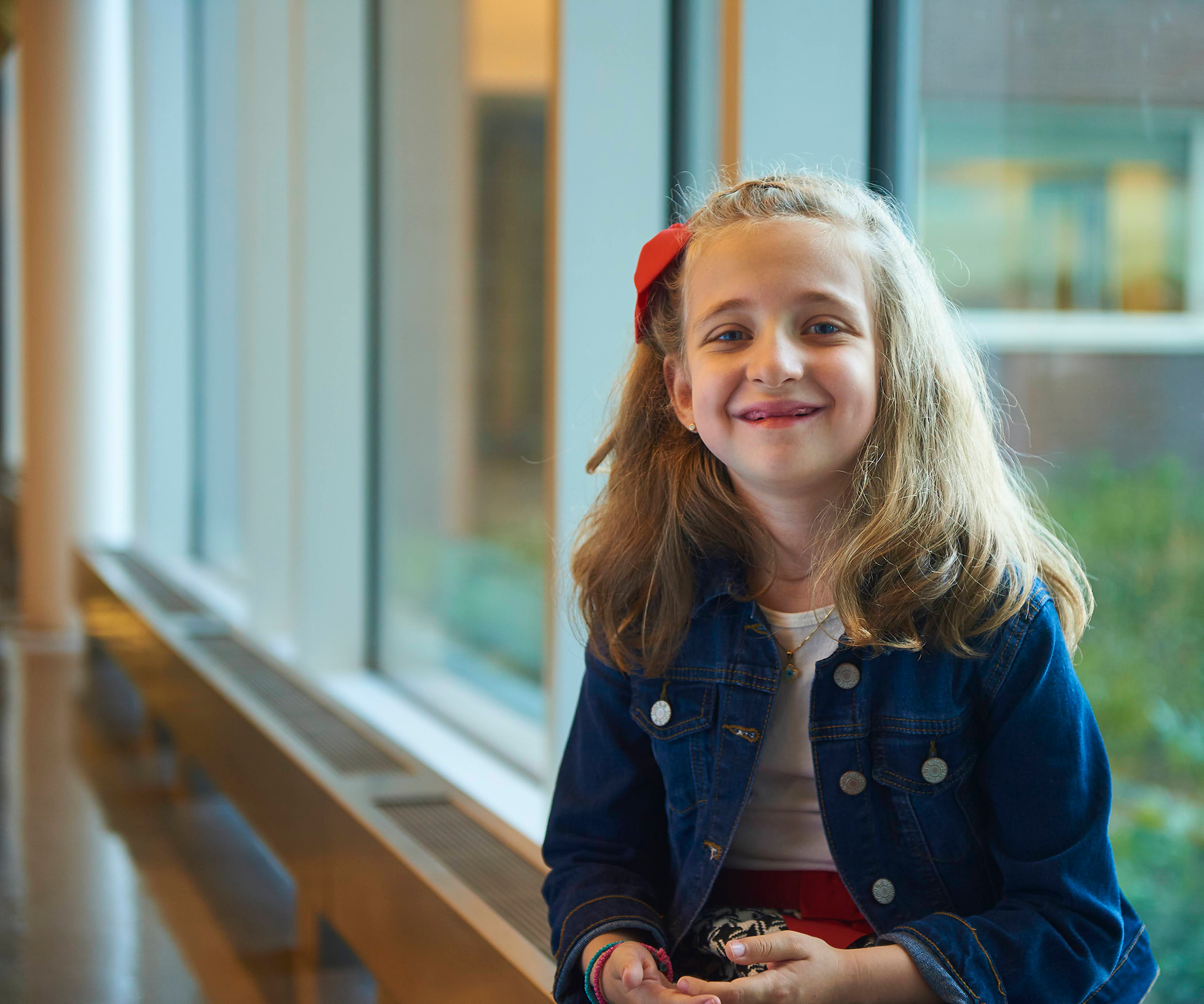little girl with long blonde hair with a red bow in it wearing a jean jacket