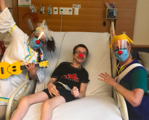 Andrew in bed with a red nose, with the therapeutic clowns posing by his bedside.