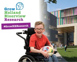 A young boy who uses a wheelchair and wearing a red tshirt and glasses holds a model brain. Behind him is a building structure. Text reads Grow Holland Bloorview Research. 