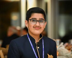 A teen with medium skin tone and short black hair wearing glasses, a blue shirt and a blue lanyard.