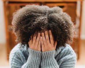 Image of young adult covering their face with their hands, hunched over