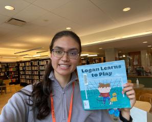 Anusha holding her book: Logan Learns to Play.