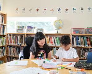 A child using wheelchair on the left, with another child on the right, reading books in a library setting