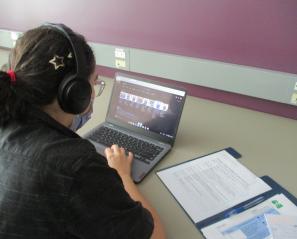Student with headphones working on a laptop with an open notebook.
