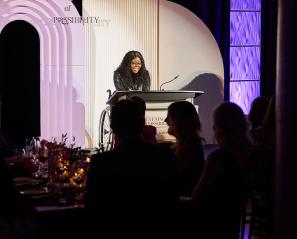 An adult giving speech to some audiences at a dark indoor setting