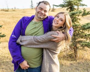 Woman with long light brown hair wraps arms around man wearing a green t-shirt and purple sweatshirt