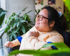 A young woman who uses a powerchair smiles and looks out a window