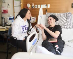 An young person sitting on a hospital bed holds hands with an adult.