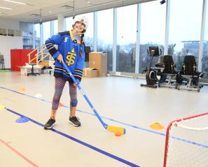 A child holding a hockey stick in front of a hockey net, wearing a helmet and ankle brace.