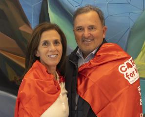 Two adults wearing red capes and standing in front of a colourful wall.