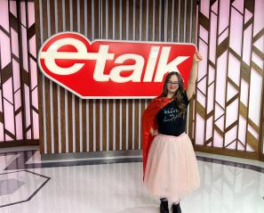 A teenager with a red cape on standing in front of a big "e-talk" logo