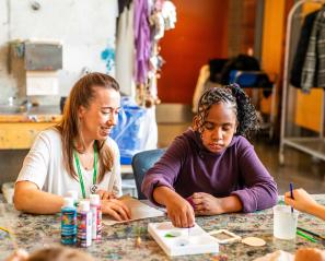 Tayah and a staff member seated at a table, painting