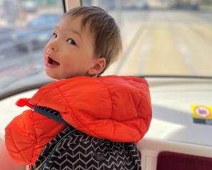 James standing at the front of a streetcar, behind the window, looking over his shoulder