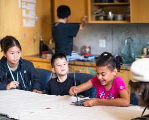 A teenager is teaching two children to draw
