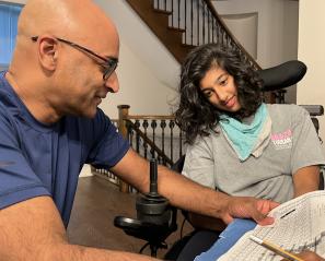 Bald man with glasses goes through a homework sheet with teen with dark hair in wheelchair