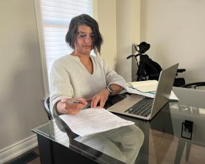 Woman with dark hair in front of laptop and papers.