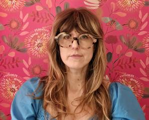 Woman with long hair and glasses against a pink wallpaper