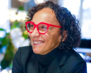 Woman with black curly hair and red glasses smiles to the side