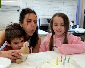Woman inbetween a girl and boy blowing out candles on a cake