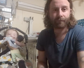 Man with beard beside child in stroller in hospital room with medical equipment