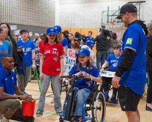 A kid on wheelchair accompany with some adults in a basketball courtyard