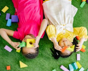 Young girls lie on floor playing with blocks