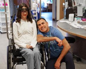 An adult with a teenager who is sitting on a wheelchair