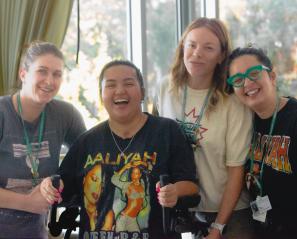 Teen wearing bright shirt and using walker surrounded by three women