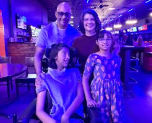 Girl in wheelchair with another girl beside her and man and woman behind in bowling alley