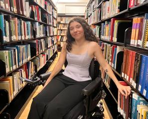 A young person who uses a wheelchair in between two library bookshelves