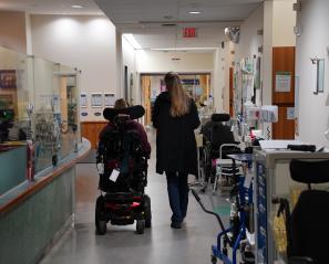 Young woman in wheelchair and woman with blonde hair walk through a hospital corridor