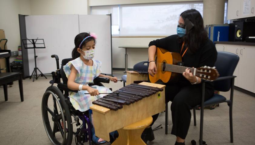 Young girl playing the xylophone and therapist playing the guitar. 