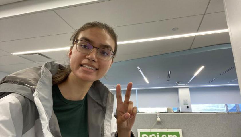 Anusha making a peace sign in front of PRISM lab sign.