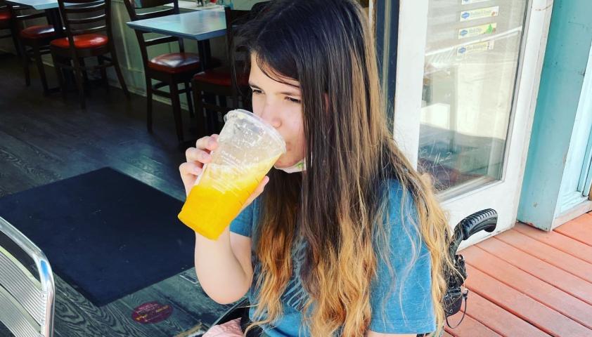 Person who uses a wheelchair drinking an orange drink.