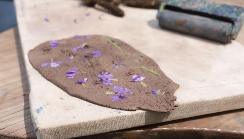 clay art project that appears to be flat and grey-ish brown, with purple flowers pressed in.