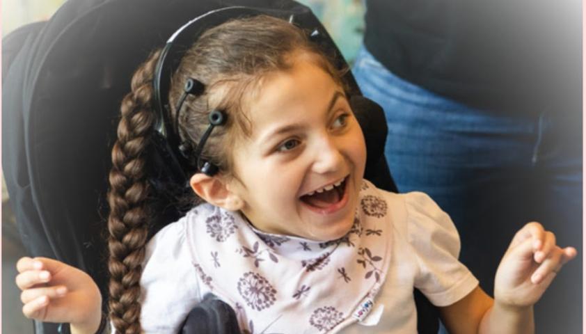 A child who uses a wheelchair smiles and uses a brain-computer interface.