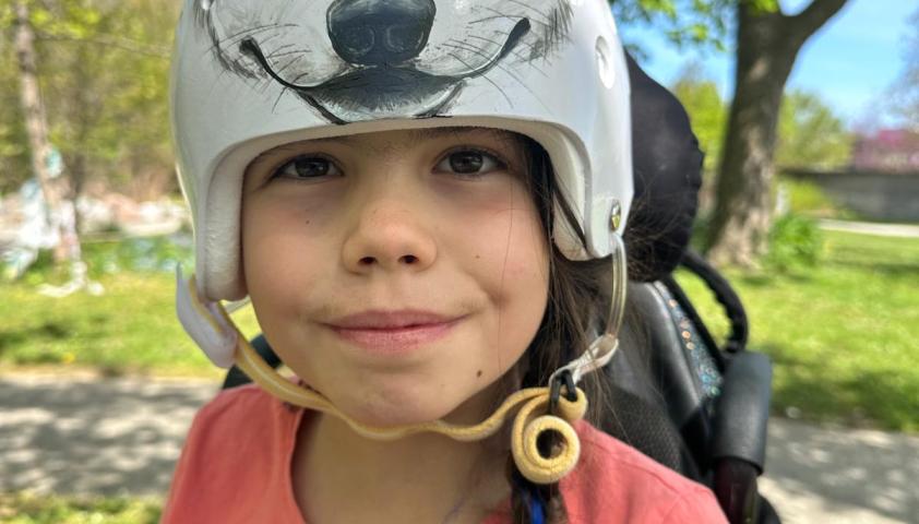 A child wearing a helmet with a wolf painted on it, sitting outside and smiling.