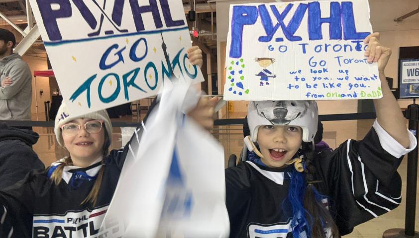 Two children holding up signs at a hockey game.