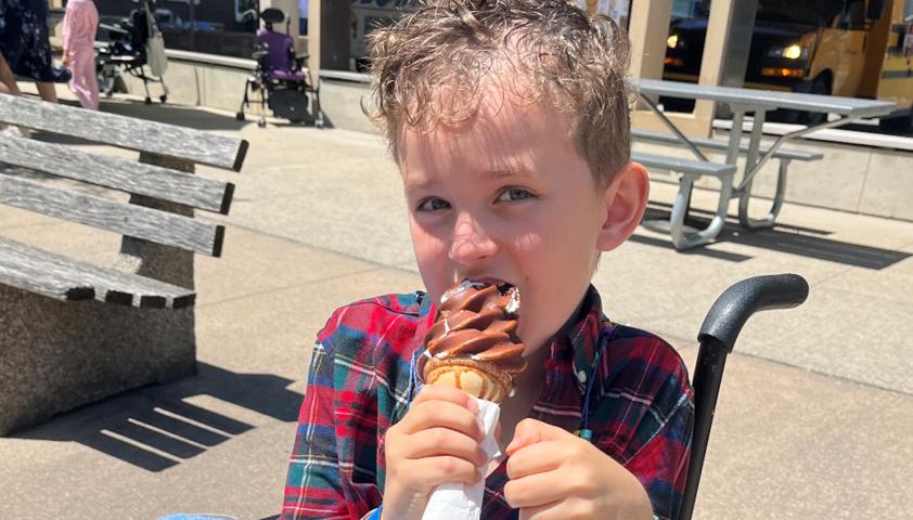 A young boy enjoys ice cream while sitting outside in his wheelchair.